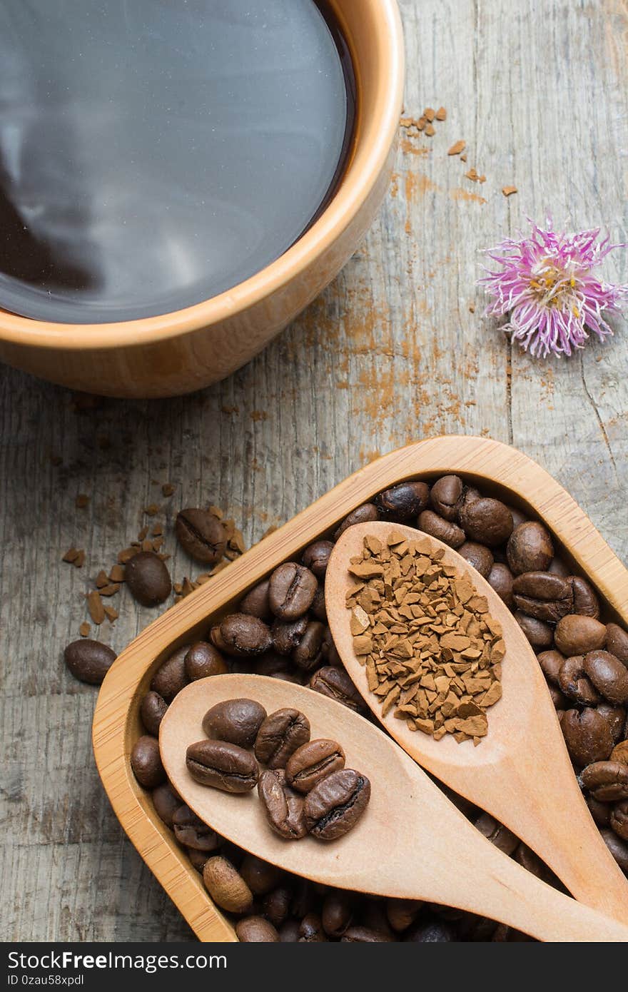 Black coffee in a cup and coffee beans in a wooden spoon on a wooden table.