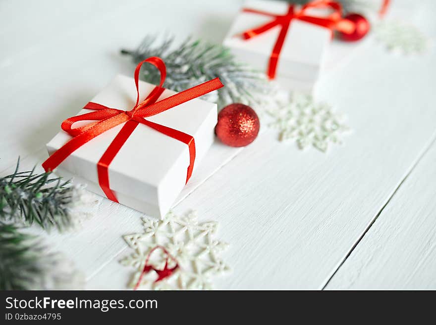 Christmas gift box, fir tree branches, red decorations on white wooden background