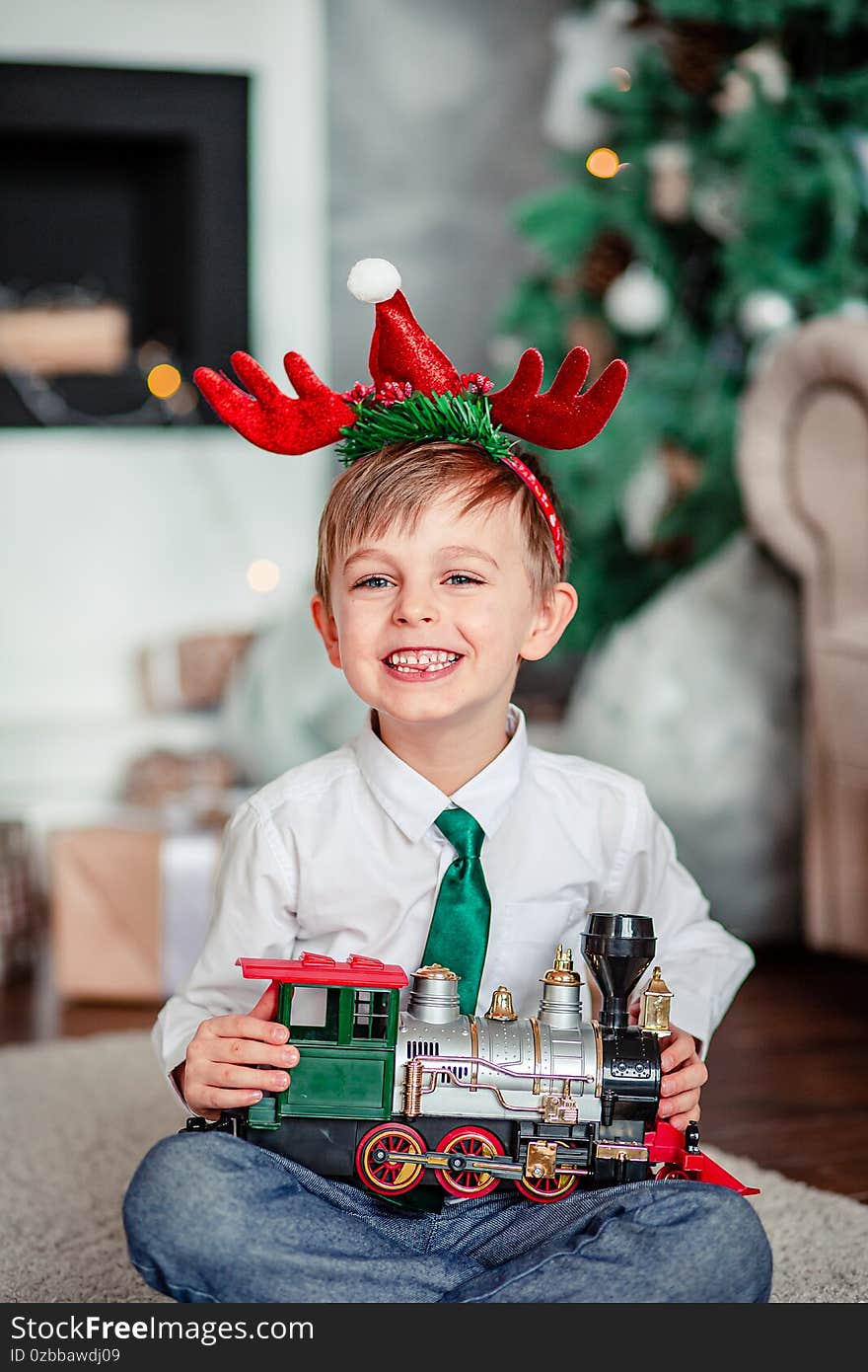 Good morning. Happy little boy with a gift, toy train, under the Christmas tree on New Year`s morning. Time to fulfill wishes