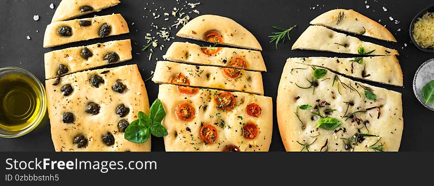 Italian Focaccia Bread with various fillings on black background. Fresh baked focaccia with tomatoes, olives, garlic and herbs, top view, banner