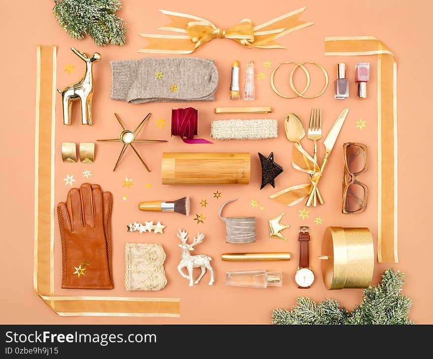 Christmas objects and gifts laid out in the shape of a gift box decorated with golden ribbon and bow. Feminine accessories and cosmetics as a gifts guide for her. Overhead view, flat lay. Christmas objects and gifts laid out in the shape of a gift box decorated with golden ribbon and bow. Feminine accessories and cosmetics as a gifts guide for her. Overhead view, flat lay.