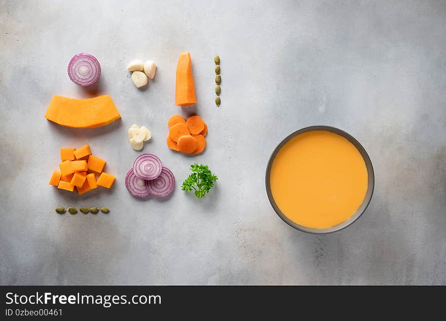 Dark bowl with pumpkin soup with seeds, spices and parsley on gray background with food ingredients. Traditional fall or winter food. top view. copy space. food knolling