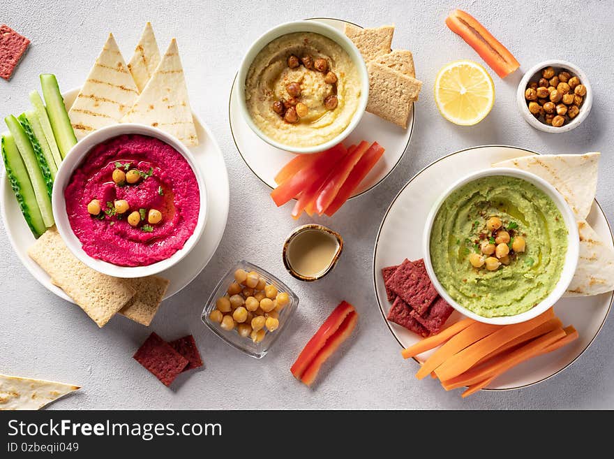 Various hummus dips in bowls, served with fresh vegetables and crisps. Traditional hummus, beetroot hummus and avocado hummus. vegetarian party food concept. top view.