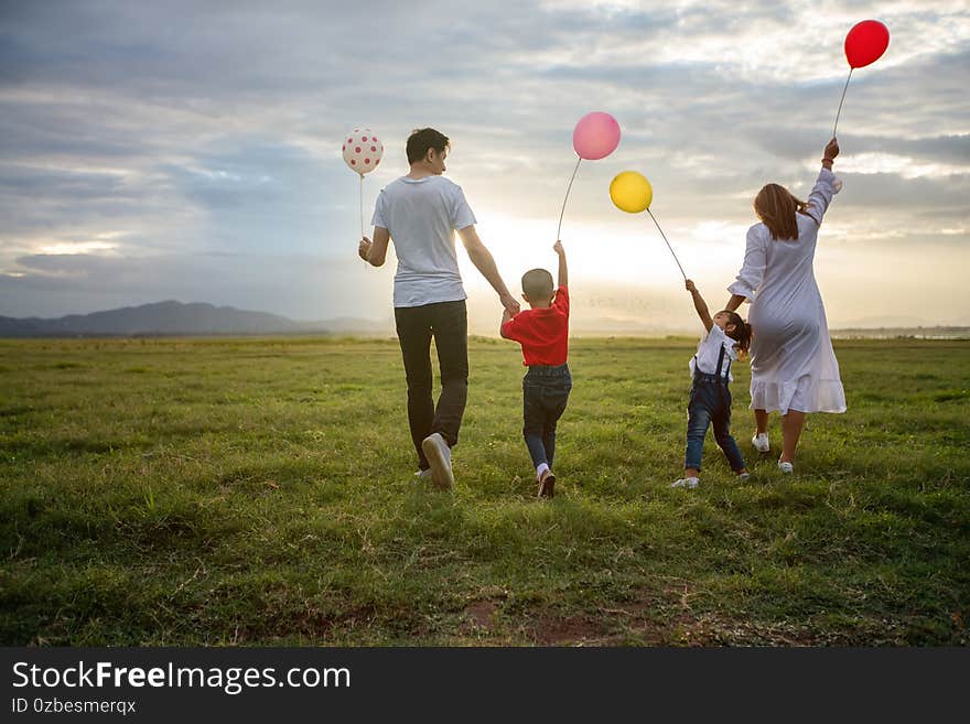 Asian family holding balloon and walking on the Meadow at sunset with happy emotion. Family Holiday and Travel concept.