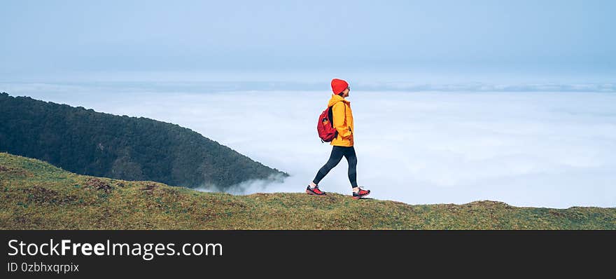 Young female backpacker dressed orange waterproof jacket hiking by the mountain above the cloud route at the end of February on