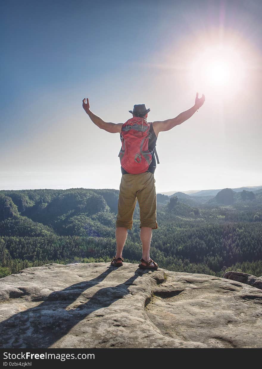 Happy hiker with red backpack  raised hands standing on a rock. Pure nature long canyon and blue sky background. Happy hiker with red backpack  raised hands standing on a rock. Pure nature long canyon and blue sky background