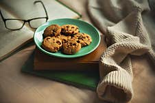 A Green Plate Of Chocolate Homemade Cookies Are On Top Of A Stack Of Old Books, Next To An Open Book And A Thick Warm Sweater. Stock Image