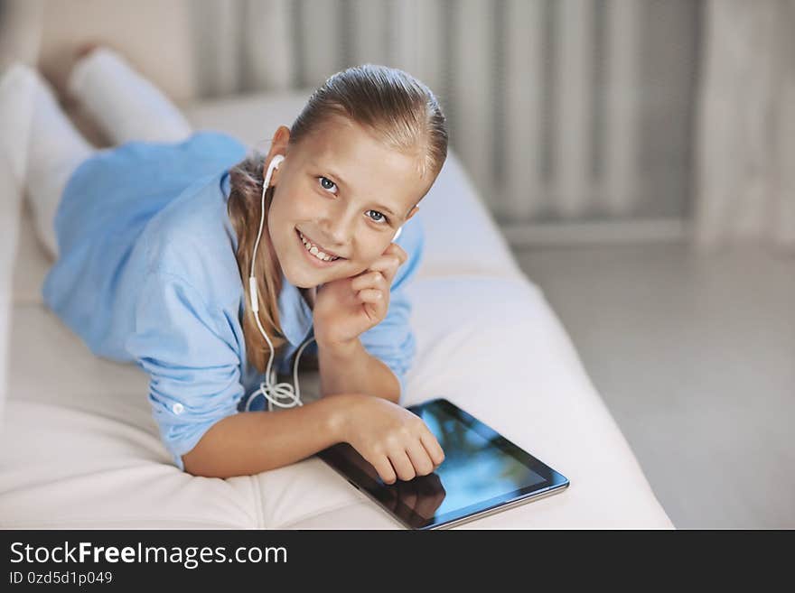 Blonde teenage girl lying on the couch plays a game on the tablet and communicates via video link with friends. Digital