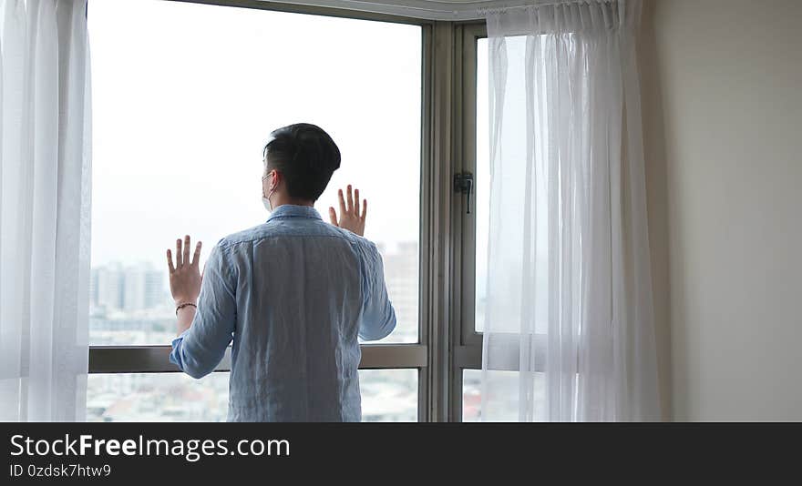 Back view of asian young man wearing face mask stay isolation at home for self quarantine due to epidemic of COVID-19  . Back view of asian young man wearing face mask stay isolation at home for self quarantine due to epidemic of COVID-19  .