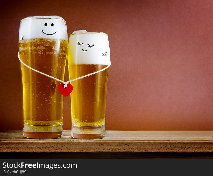 Two glasses of beer with Painted happy couple and red heart on a string. Valentine day, happy couple concept. Copy space. Two glasses of beer with Painted happy couple and red heart on a string. Valentine day, happy couple concept. Copy space