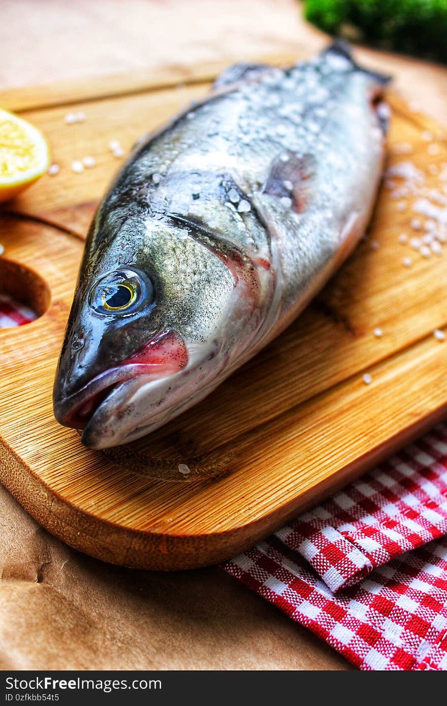 One raw fish on a wooden chopping Board is decorated with a lemon slice in close-up.Texture or background. One raw fish on a wooden chopping Board is decorated with a lemon slice in close-up.Texture or background