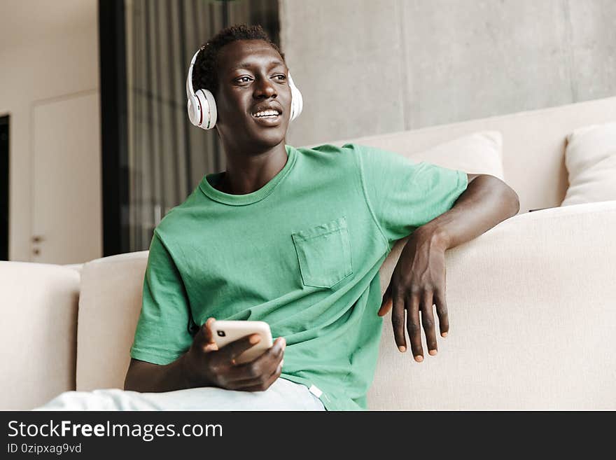Image of african american man in headphones using smartphone at home