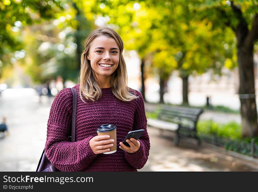 Beautiful smiling woman reading message or browsing her mobile phone while having coffee break outdoors