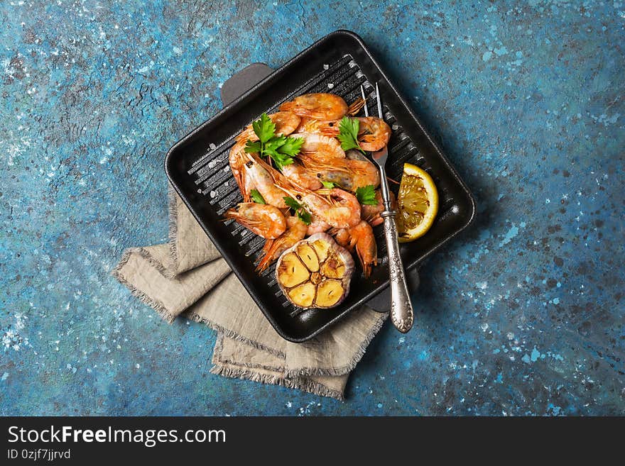 Spicy fried shrimps on grill pan with lemon, garlic and green parsley