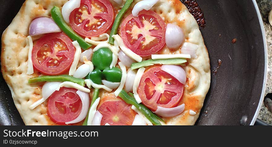 Close up top view of Indian home made pizza cream and dark golden brown color decorated with tomato, capsicum, cheese being prepared on the gas oven. Close up top view of Indian home made pizza cream and dark golden brown color decorated with tomato, capsicum, cheese being prepared on the gas oven.