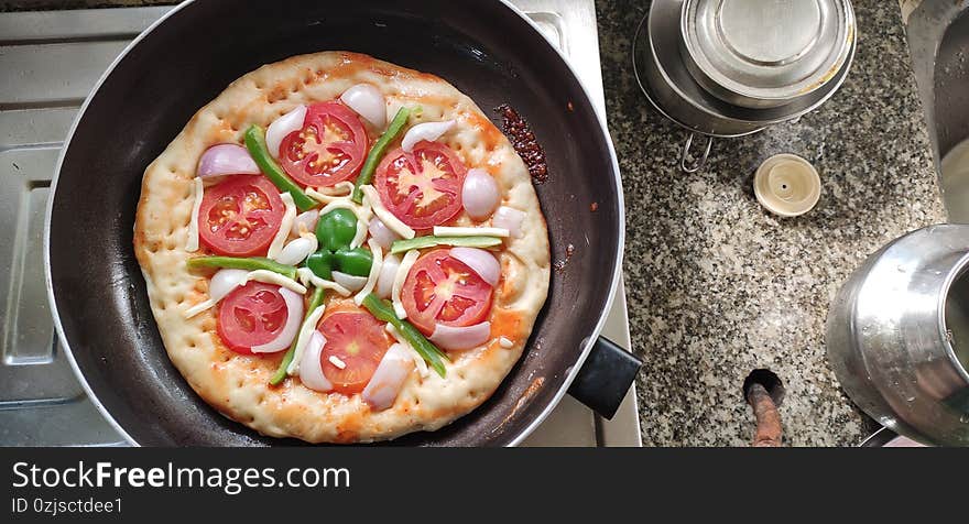 Close up top view of Indian home made pizza cream and dark golden brown color decorated with tomato, capsicum, cheese being prepared on the gas oven. Close up top view of Indian home made pizza cream and dark golden brown color decorated with tomato, capsicum, cheese being prepared on the gas oven.