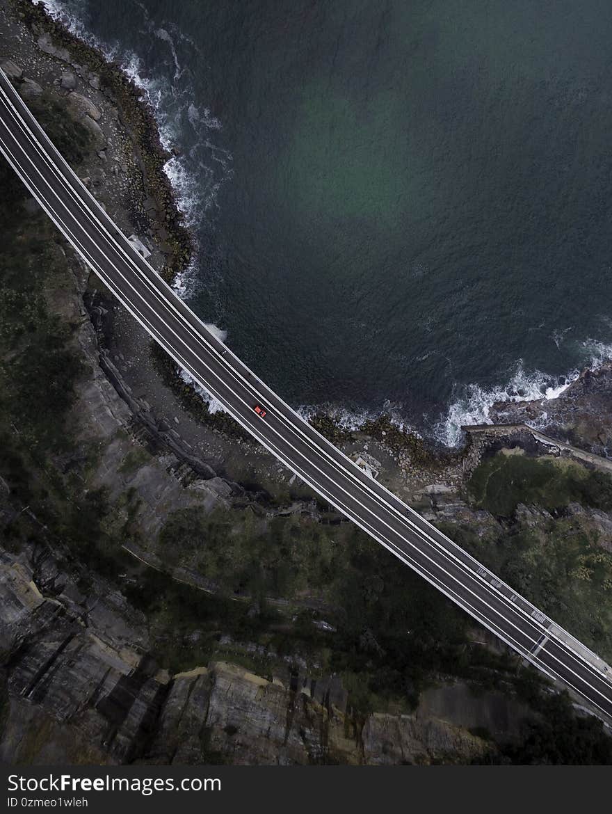 Aerial top view of a straight paved highway road with a single car running along the seashore