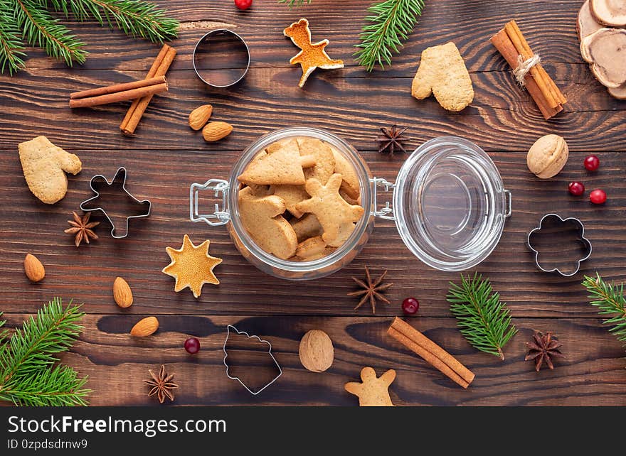 Glass jar with gingerbread among nuts and cookie cutters and fir branches