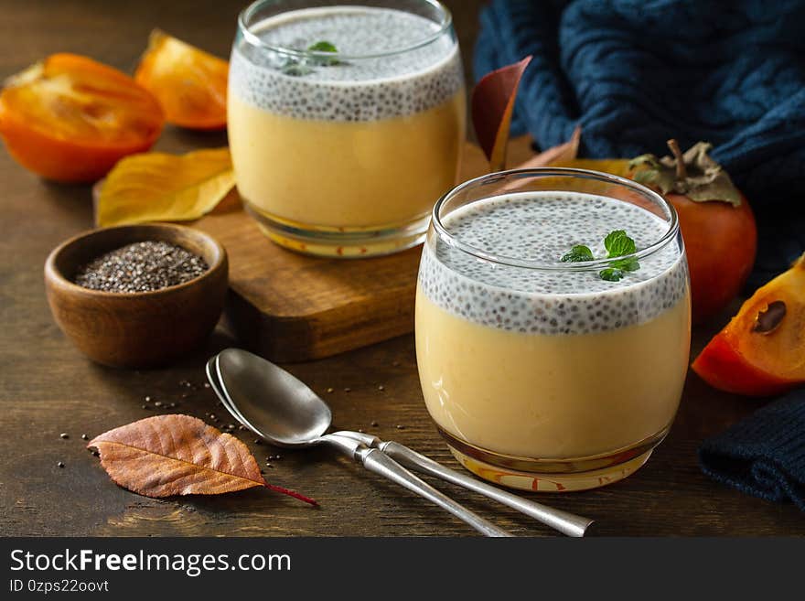 Autumn dessert. Homemade panna cotta with persimmon fruit and chia seeds on a wooden table.