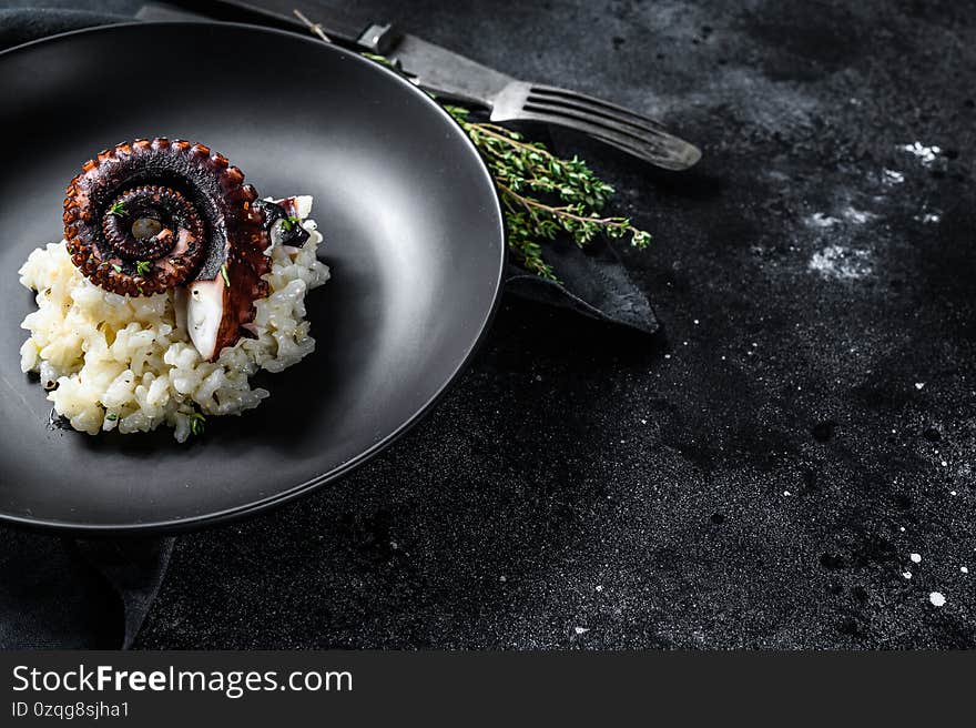 Italian classic Risotto with octopus tentacles. Black background. Top view. Copy space