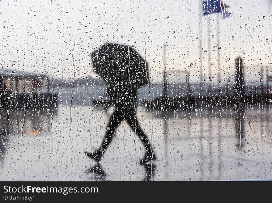 Selective focus shot of a wet window with a view of people with umbrella walking on a rainy day