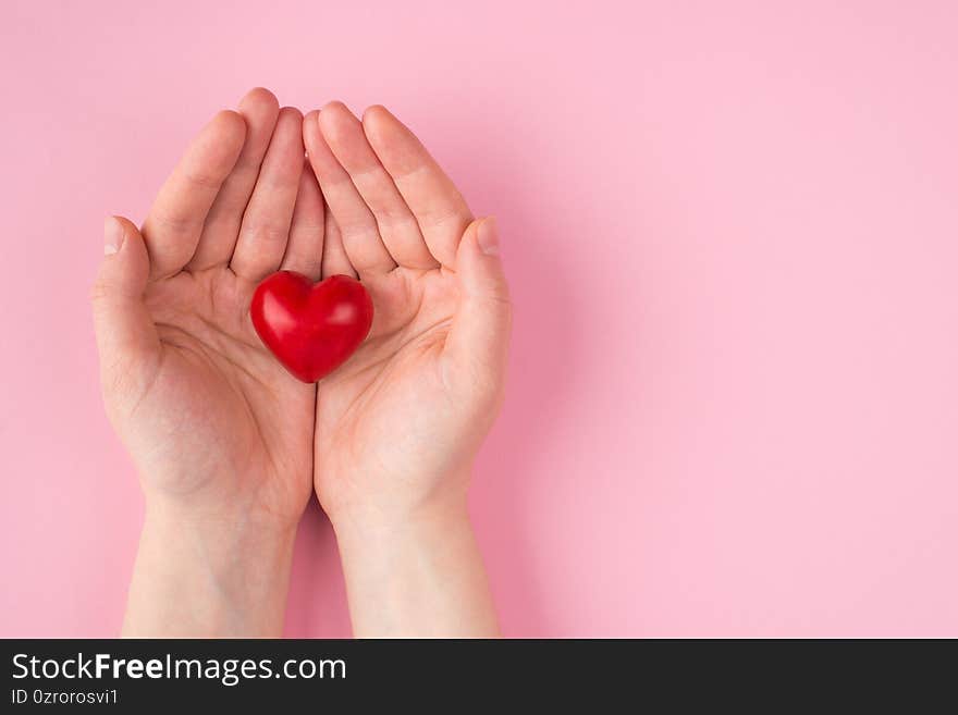 St. Valentine`s day concept. Top above overhead pov first person view photo of female hands holding a red heart to the left side isolated on pink pastel background with copyspace.