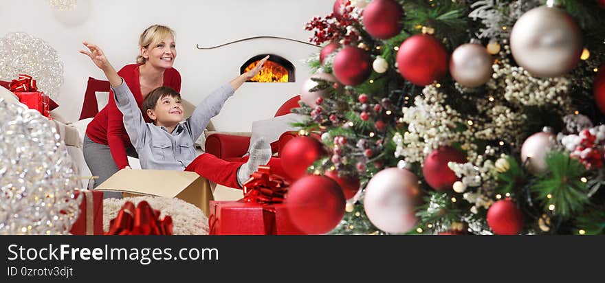 Merry christmas, happy family at home, mom plays with their son near the illuminated and decorated tree, joyful and smiling sitting in the living room and comforted by the fireplace