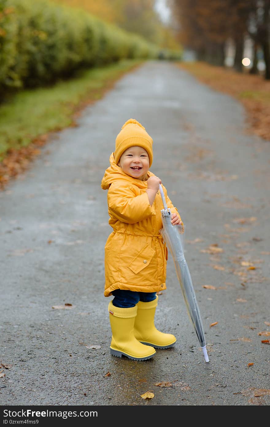 A little girl is jumping in a puddle in yellow rubber boots and a waterproof raincoat.