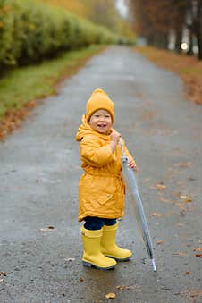 A Little Girl Is Jumping In A Puddle In Yellow Rubber Boots And A Waterproof Raincoat. Stock Images