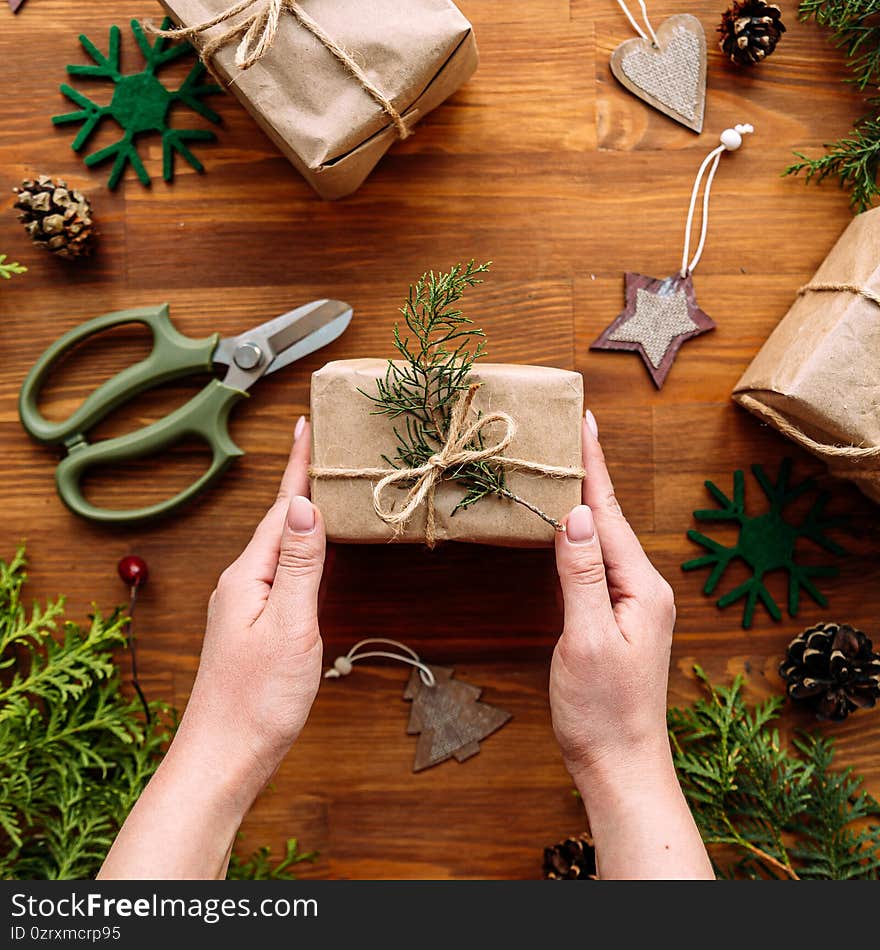 Top view on female hands holding holiday craft gift box with spruce branches on the wooden table. Top view on female hands holding holiday craft gift box with spruce branches on the wooden table