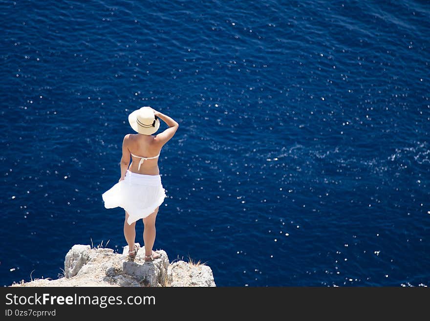 A girl in a white dress stands on a rock