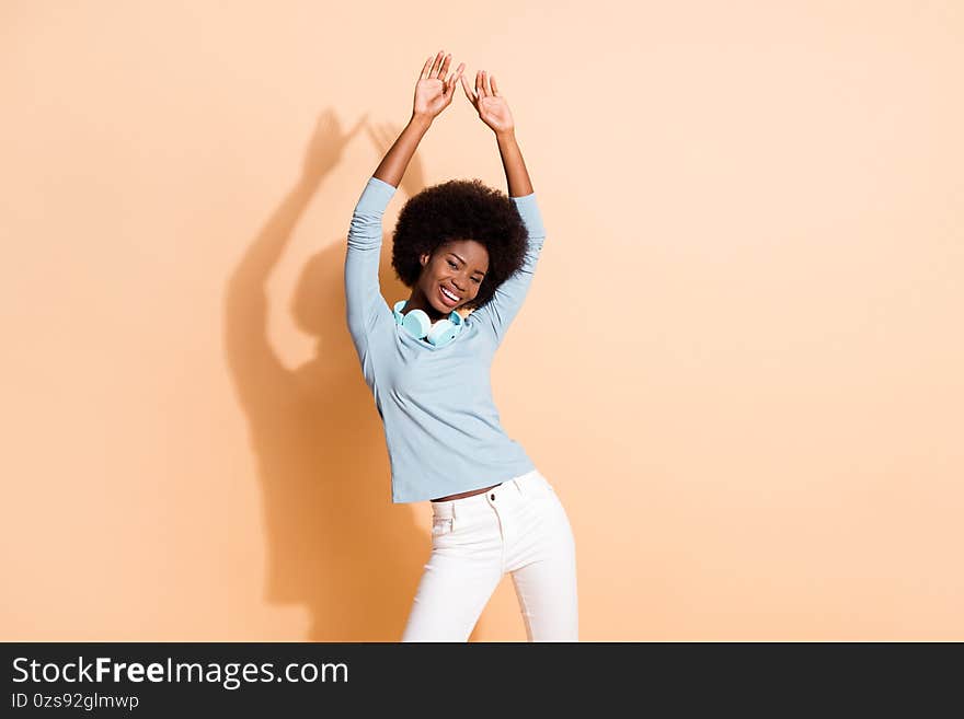 Photo portrait of african american woman dancing with both hands in air isolated on pastel beige colored background.