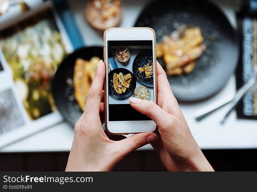 Woman taking a photo of breakfast with smartphone, hands hold phone, frome above