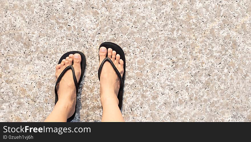 Close-up Foot in black flip flop standing on big marble texture at the beach