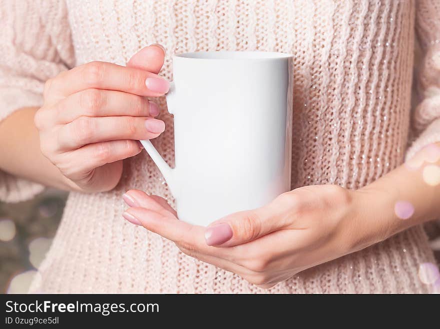 Mockup - White cup in the hands of woman in a pink winter sweater. Christmas coffee mug