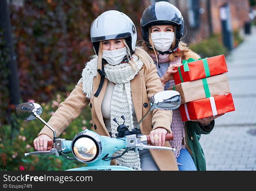 Picture of two women wearing masks and holding shopping bags commuting on scooter. Picture of two women wearing masks and holding shopping bags commuting on scooter