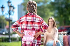 Rear View Of Girl Holding Card For Her Mom Sitting On Park Bench Stock Image