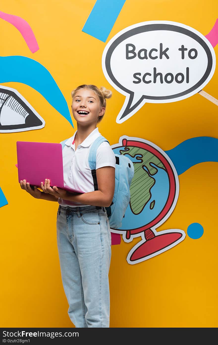 Schoolgirl holding laptop near speech bubble with back to school lettering and paper art on yellow background