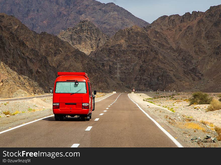 Red tourist bus on a mountain road across the desert