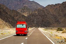 Red Tourist Bus On A Mountain Road Across The Desert Royalty Free Stock Images