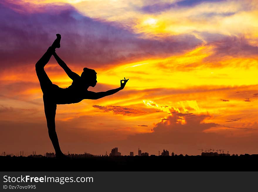 Silhouette of healthy woman practicing yoga meditation during on background city with sky and sunset