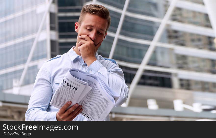 Businessman reading newspaper feeling serious standing in urban background. Handsome men holding newspaper in his hand with