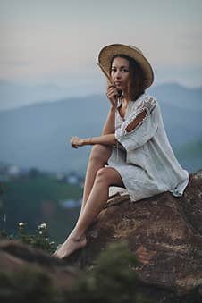 The Blonde In A Linen Dress And Straw Hat Sits On A Viewpoint In The Mountains Stock Image