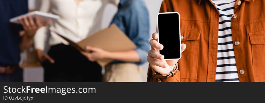 Partial view of businessman showing smartphone with blank screen near blurred colleagues on background, banner. Partial view of businessman showing smartphone with blank screen near blurred colleagues on background, banner