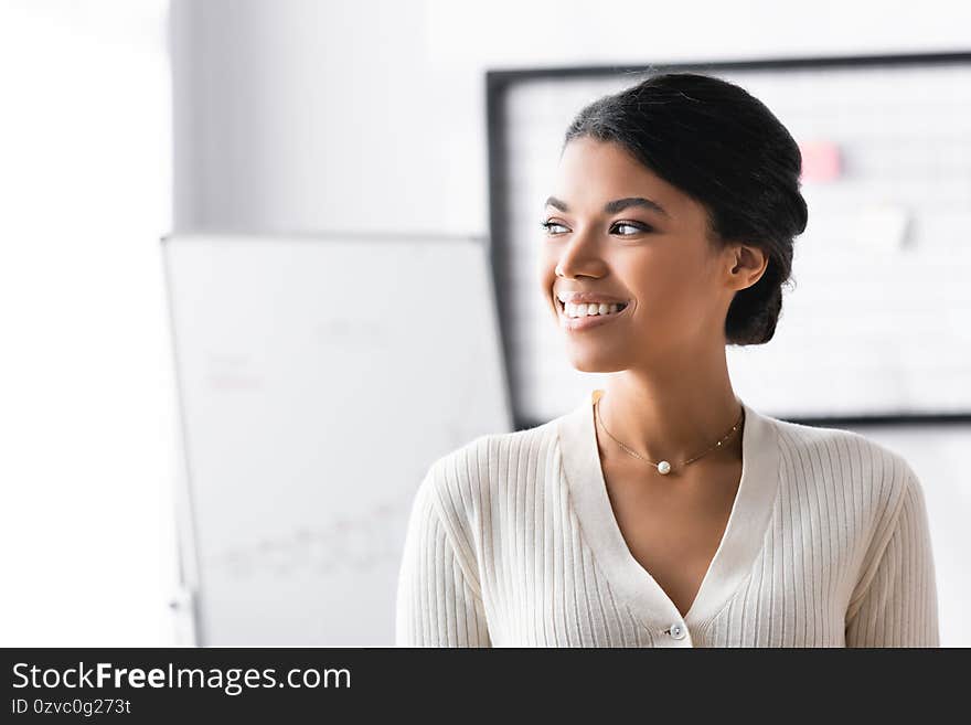 Happy african american woman looking away while standing in office on blurred background