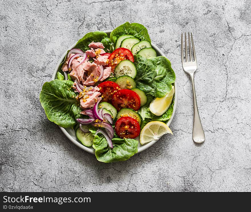 Canned tuna, tomatoes, cucumbers, romaine salad, red onion, olive oil salad - delicious healthy food on a grey background, top view.