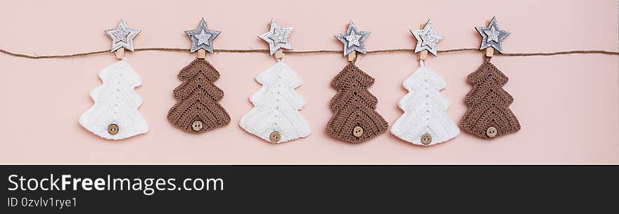 Christmas handmade. Knitted fir-trees in a row on a rope on a pastel background. Handicraft and leisure. Web banner