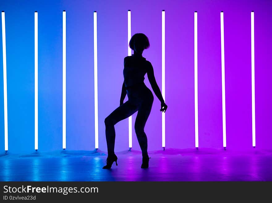 Young stylish girl dancing in the Studio on a colored background with neon lighting lamp. Music dj poster design. Dark