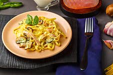 Pasta With Ham And Mushrooms In A Creamy Sauce On A Black Board And A Blue Napkin With A Fork Near The Ingredients Stock Photography