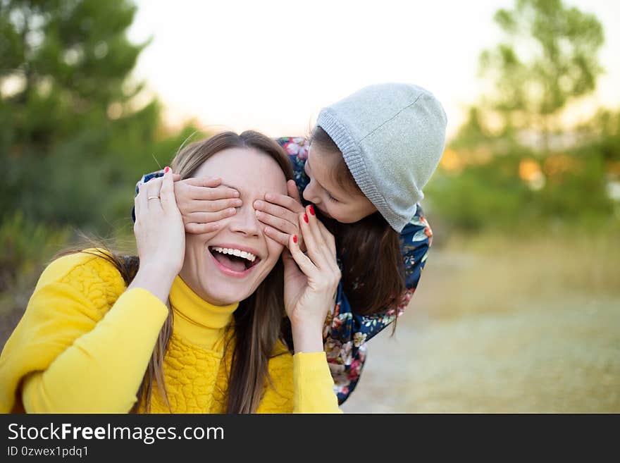 Happy young girl laughing, covering eyes of her mother with her hand.